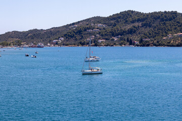 Skiathos, Greece A picturesque marina featuring boats docked by a tranquil coastal town, set against rolling hills under clear blue skies. Ideal for travel and tourism themes.