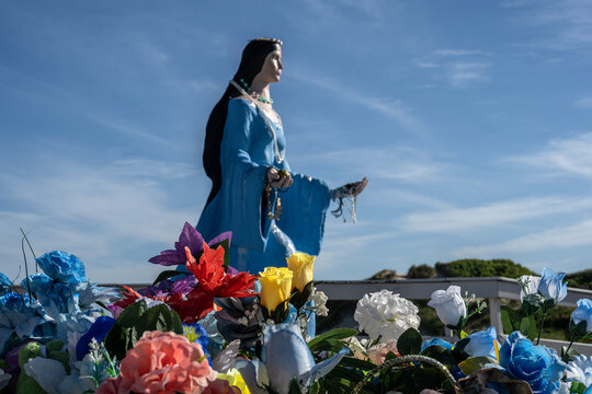 Statue of Yemanja, goddess of the sea, with flowers in the foreground on a sunny day.