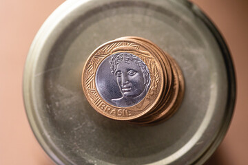 Real, moeda brasileira. Uma pilha de moedas de 1 Real sobre um cofrinho de pote de vidro. Verso da...