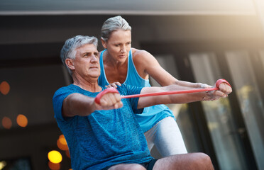 Fitness, physical and resistance band with elderly couple in home together for strength training. Exercise, stretching or workout help with senior man and woman in apartment for retirement health