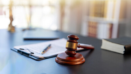 A wooden gavel sits on a desk next to a stack of books and a clipboard