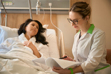 Woman doctor with history of patients illness sits near bed