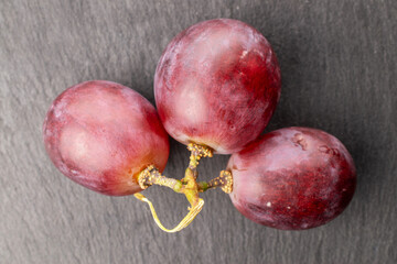 Three grape berries on slate stone, macro, top view.