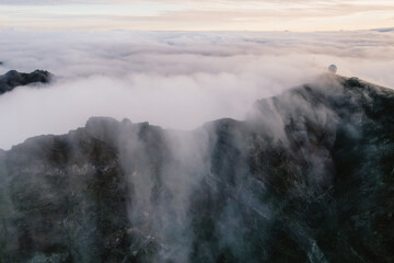 Aerial view of majestic mountain ridges at sunrise with falling fog from top of Pico do Areeiro, Madeira island, Portugal
