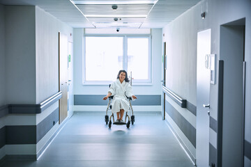 Woman in a fluffy robe sits in a wheelchair in a hospital corridor