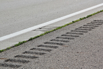 Safety rumble stripe and white markings on the gray road pavement or highway. Close up view of the texture on the surface.