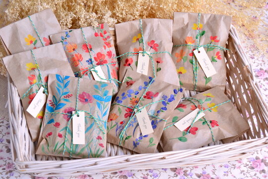 Wedding favors original packaging craft paper bags with hand painted watercolor flowers pattern, ribbon decoration and custom thank you label, wicker basket on favour table, diy handmade guest gifts