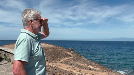 Happy carefree elderly man enjoying travel and sunny day at sea, relaxed bearded male in vacation or retirement admiring the seascape and horizon over water