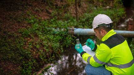 An ecologist in a green jacket sitting aside the pond try to  examination the quality of water  in...