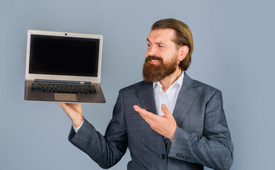 Bearded business man in suit showing laptop computer with blank mockup screen. Smiling programmer, IT specialist, ceo presenting open notebook with empty mock-up screen. Copy space for advertising.