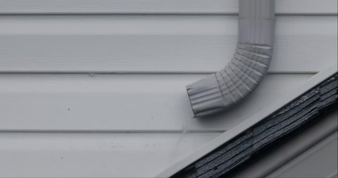 A metal gutter, overflowing with rainwater, streams down a home during a heavy downpour. The gutter seems firmly attached to the building&rsquo;s exterior wall.