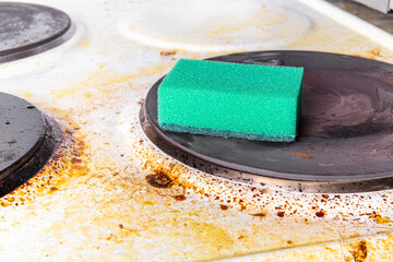 Dirty electric stove and green cleaning sponge. Grease spots. Cleaning the kitchen. Cleaning the stove from grease