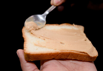Toast with peanut butter and a spoon in hand on a black background