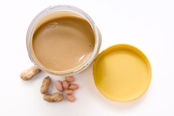 Peanut butter in a jar and peanuts on a white background