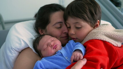 Mother and her children, a newborn and a big brother, sharing a tender family moment in a hospital setting. The image highlights love, warmth, and the bond between siblings