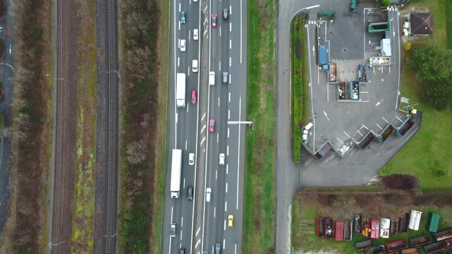 Aerial view of a busy highway with trucks running parallel to railway tracks and an industrial facility