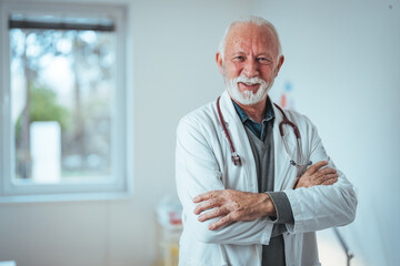 A confident senior Caucasian male doctor stands in a clinical setting, arms crossed, dressed in a white coat with a stethoscope, embodying professionalism and experience.