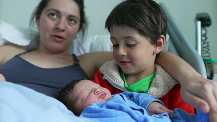 Obraz premium Mother watches lovingly as older sibling cradles newborn baby, highlighting the tender bonds of family love, affection, and the nurturing connection between siblings in a heartfelt moment