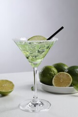 Delicious Margarita cocktail with ice cubes in glass and lime on white table