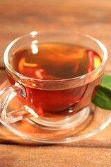 Aromatic tea in glass cup and green leaves on wooden table, closeup