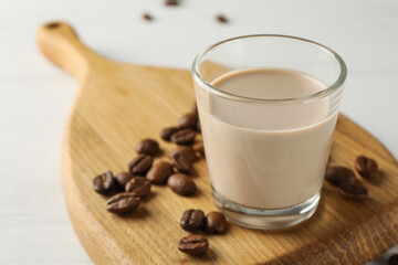 Coffee cream liqueur in glass and beans on white table, closeup