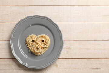 Heart made of tasty spaghetti on wooden table, top view. Space for text