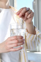 Woman putting effervescent pill into glass of water indoors, closeup