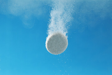 Effervescent pill dissolving in water on light blue background, closeup