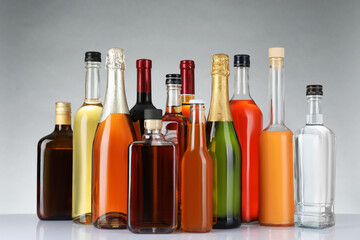 Bottles of different alcoholic drinks on white table against light background