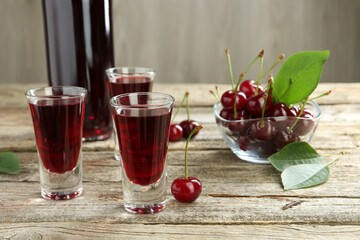 Bottle and shot glasses of delicious cherry liqueur with juicy berries on wooden table