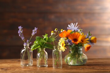 Different flowers in glass bottles on wooden table