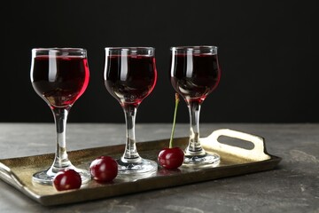 Delicious cherry liqueur in glasses and fresh berries on grey table