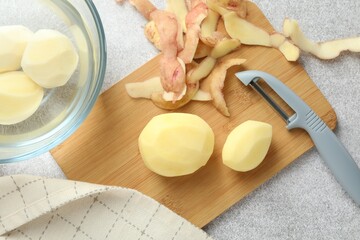 Fresh raw potatoes, peels and peeler on light grey table, top view