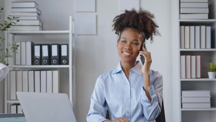 Confident businesswoman happily talking on the phone while working at her desk in an organized office setting. Engaged in a lively conversation, showcasing professionalism and multitasking skills