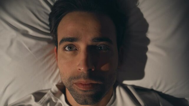 Thinking man lying pillow looking up at night closeup. Calm unshaved guy resting