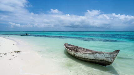 Naklejka premium An old wooden boat sits on a pristine white sandy beach with crystal clear turquoise ocean water, under a bright blue sky with majestic clouds in a tranquil setting