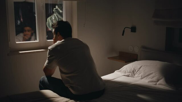 Depressed guy sitting bedding by window at night feeling anxious. Pensive man 