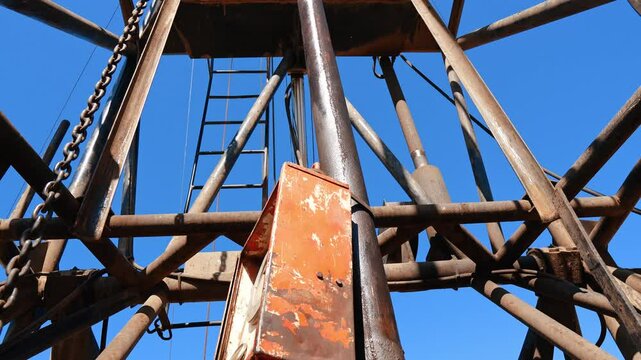 Standing under and looking up at the high tower of a drilling site. Equipment used for resources production.