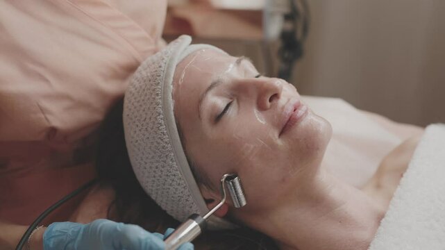 A relaxed woman enjoys a microcurrent facial treatment at a wellness spa, with a professional using specialized equipment.