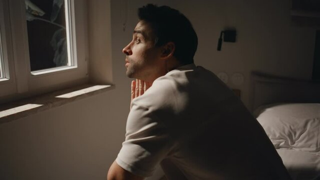 Man looking night window bedroom feeling depression closeup. Worried guy on bed