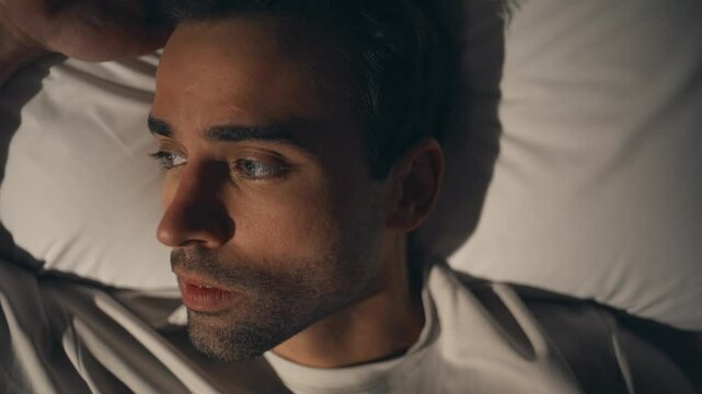 Sad man resting night apartment lying on bed showing calm expression closeup.