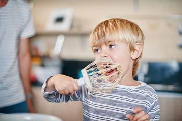 Child, lick and whisk in home while baking with mouth or tongue for learning, eating and youth as development. Boy, taste and batter in kitchen while cooking with recipe for cake, cookies or teaching