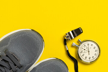 Sport equipment. Sneakers, whistle and stopwatch on yellow background.