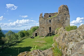 Hrad Přimda stands tall atop a hill, its ancient ruins glowing under a bright blue sky on a summer day.