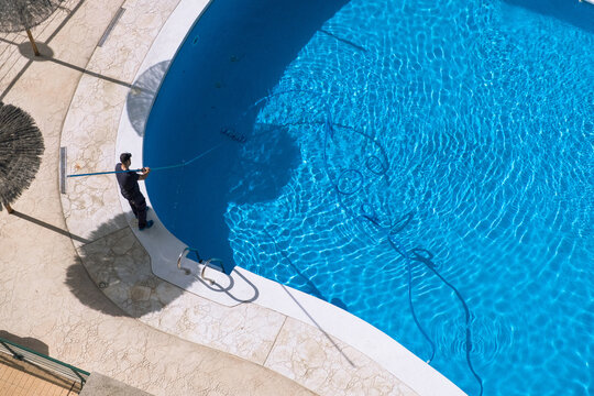 Cleaning and maintenance of swimming pool. Aerial view to maintenance person cleaning swimming pool in sunny day