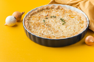 Homemade onion cake on the yellow background. Traditional quiche pie with steamed onions, cheese and bacon