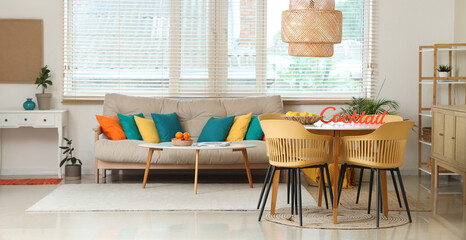 Interior of stylish living room with cozy sofa, basket with fruits on dining table and window