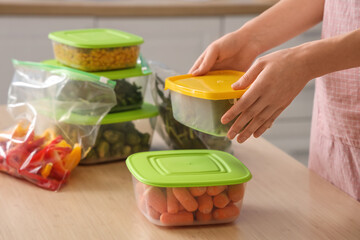Woman stacking plastic containers with vegetables for freezing on wooden table