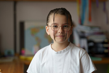 Fototapeta premium Little beautiful teenage girl in glasses with a hairstyle. Blurred children's room in the background. Childhood concept