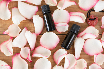 Rose petals and rose essential oil in glass bottle lying on the table, top view.